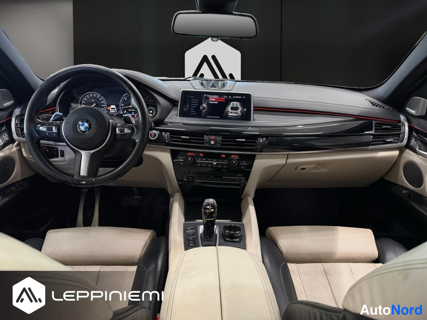 Muu: Auton ohjaamo näkyy keskeltä: BMW-ohjauspyörä, kojelauta ja infotainment-näyttö, vaaleat penkit ja keskitaso_automaattivalitsimella.