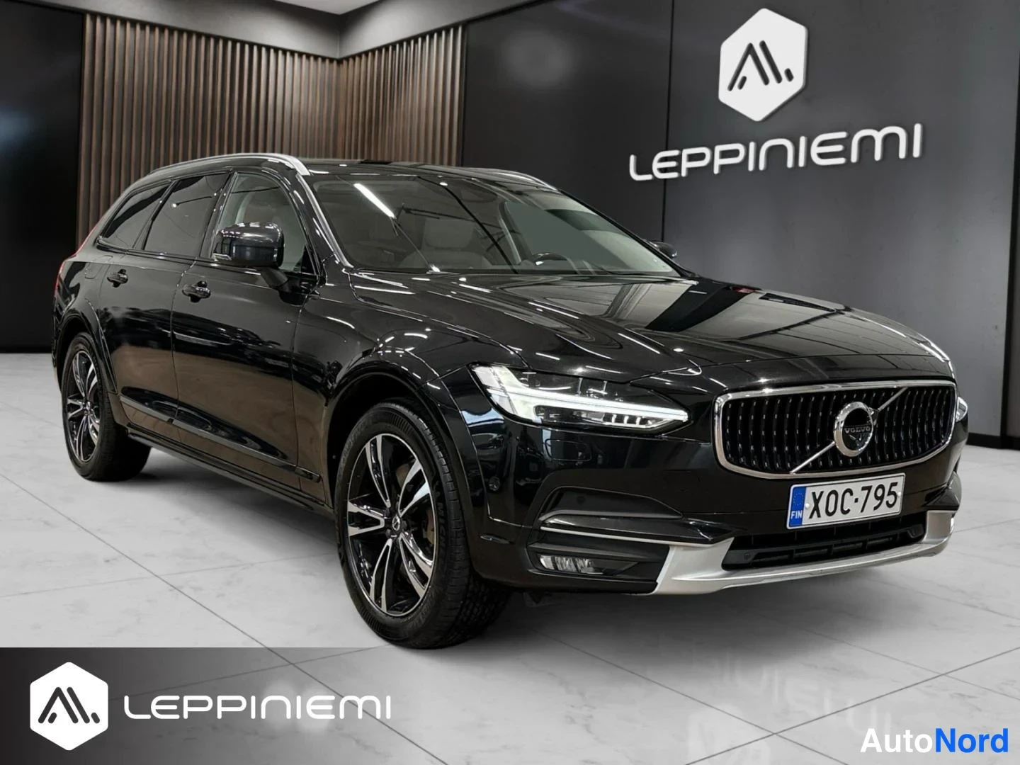 Etuviisto, nokka vasemmalle: Musta Volvo V90 Cross Country -farmari kulmassa edestä vasemmalta nähtynä sisätiloissa.
