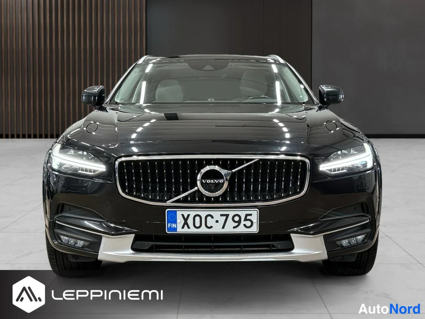 Edestä: Mustan Volvo V90 -auton etupää suoraan edestä kuvattuna, rekisterikilpi.
