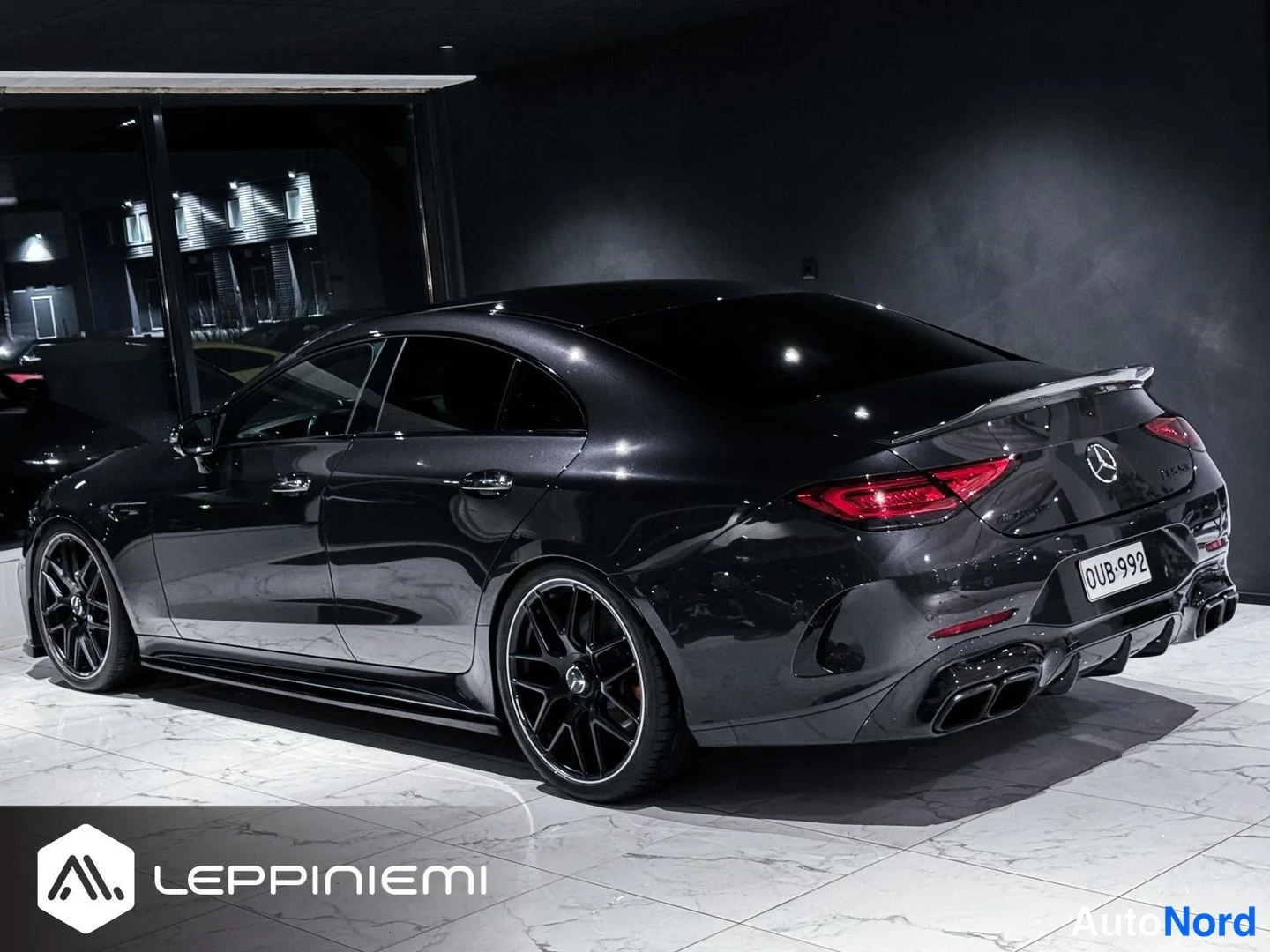Takaviisto: Mustanharmainen Mercedes-Benz CLS takaa- ja sivulta kuvattuna tummassa sisätilassa; takavalot, AMG-takapuskuri ja neljä pakoputkea näkyvät, rekisterikilpi.