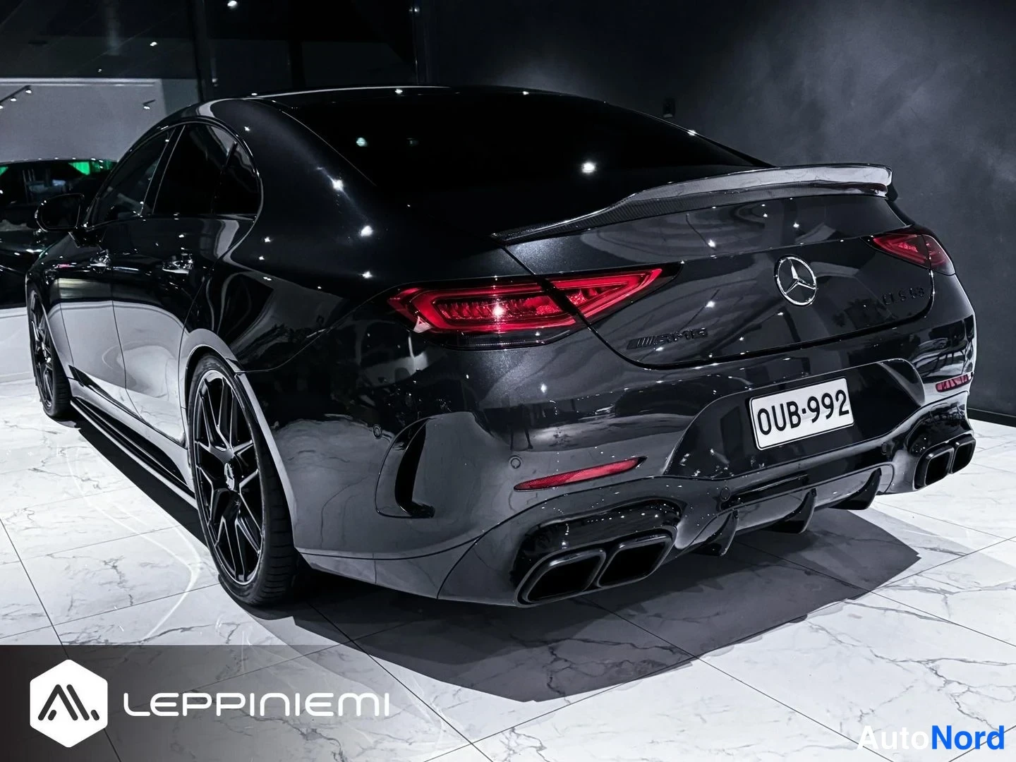 Takaa: Mustanharmainen Mercedes-Benz CLS suoraan takaa kuvattuna; AMG-merkintä, takavalot, hiilikuidun värinen spoileri ja neljä pakoputkea näkyvät, rekisterikilpi.