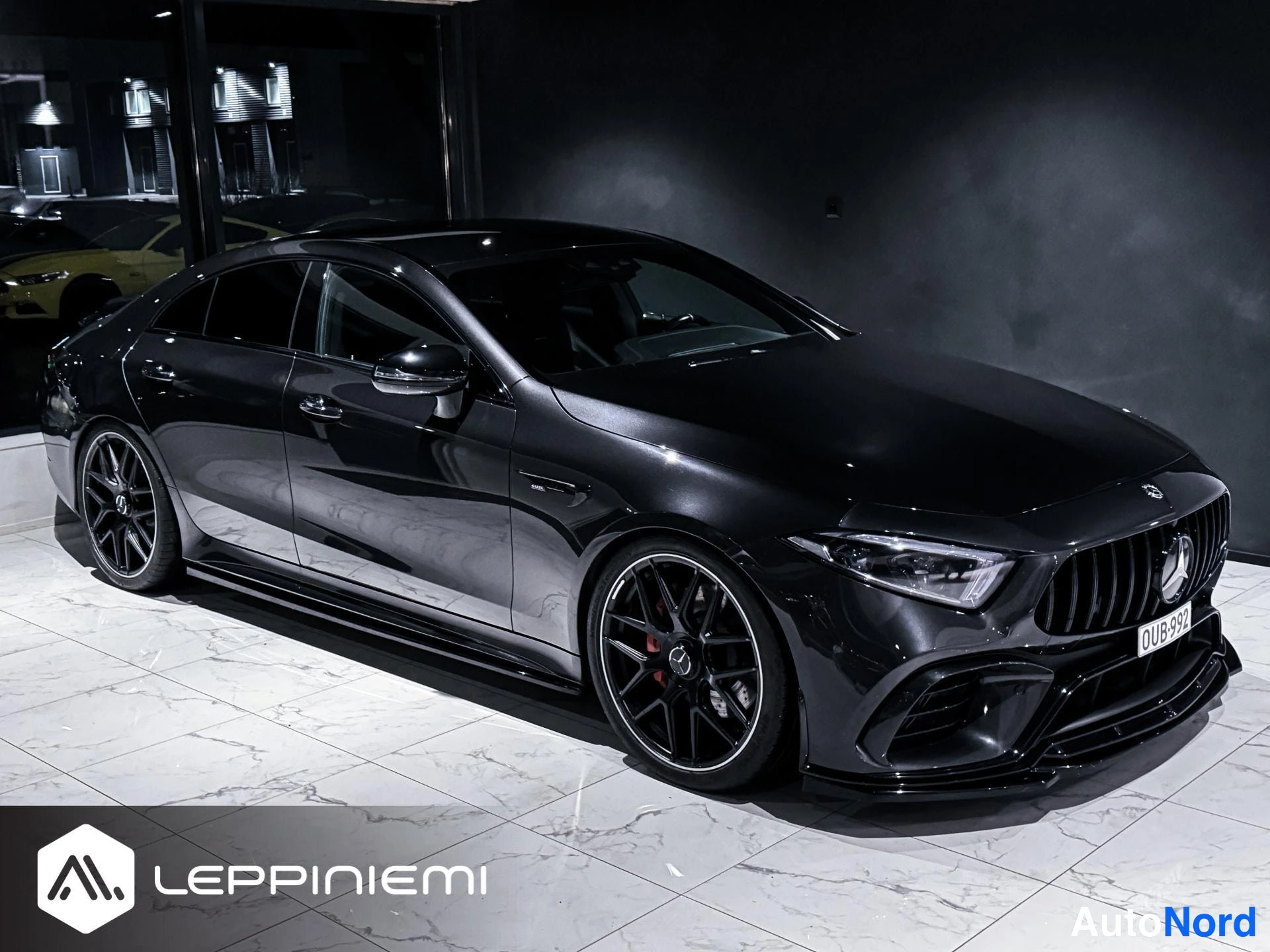 Etuviisto, nokka oikealle: Musta Mercedes-BenzCLS-tyylinen coupe etukulmasta oikealta autosalissa, keula ja vasen kylki kuvassa.