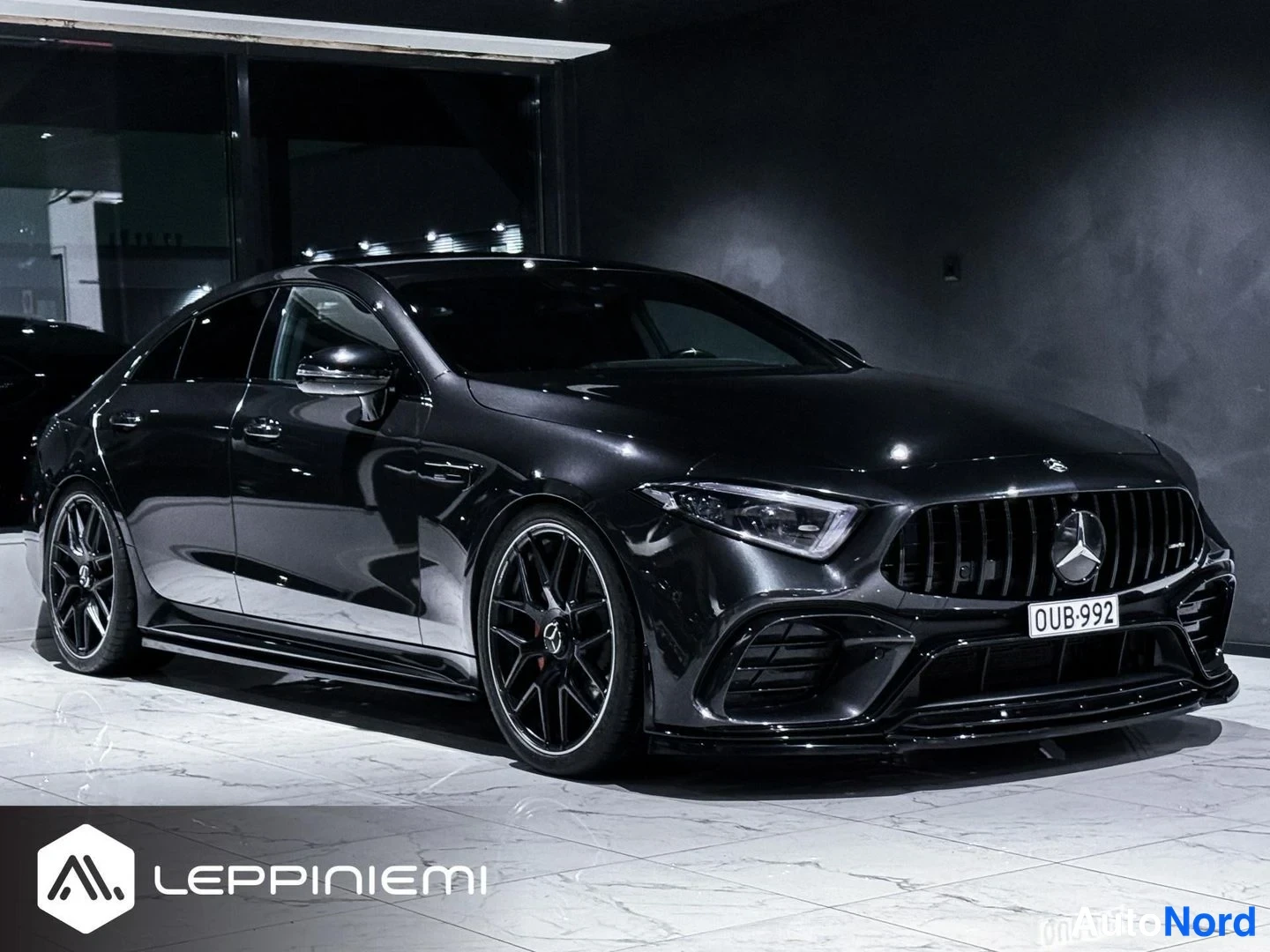 Etuviisto, nokka oikealle: Mustan Mercedes-Benz CLS -auton etukulmanäyttö showroomissa, rekisterikilpi, mustat vanteet.