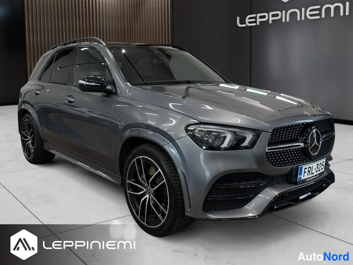 Etuviisto, nokka oikealle: Harmaa Mercedes-Benz GLE -maasturi edestä oikealta kuvattuna, AMG-tyylinen etupuskuri, mustat kevytmetallivanteet ja rekisterikilpi.