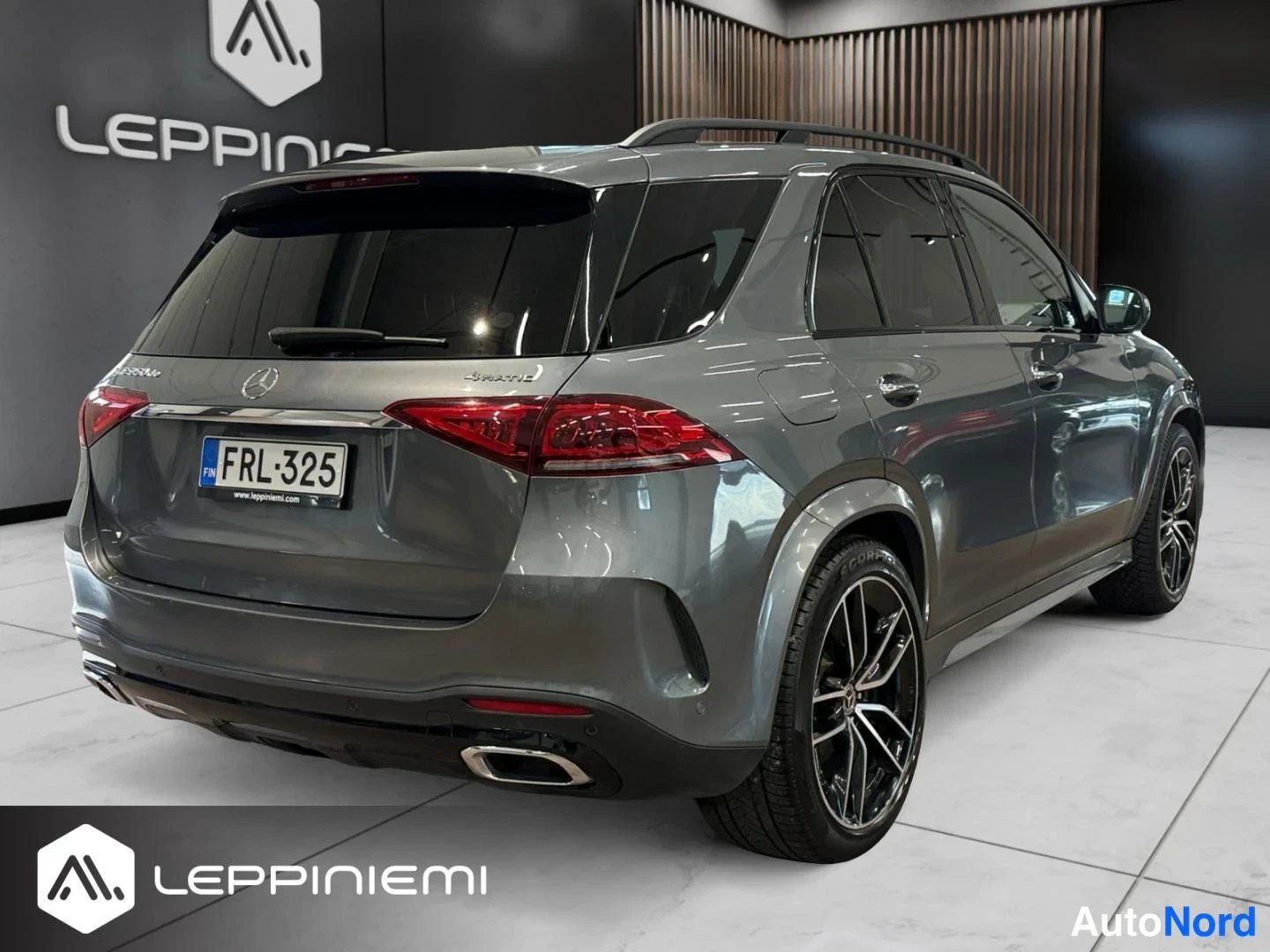 Takaviisto: Mercedes-Benz GLE:n takaosan kolmannesvasen näkymä: harmaakorinen SUV, jonka takavalot, -rekisterikilpi, kattokaiteet ja mustat vanteet näkyvät sisätiloissa.