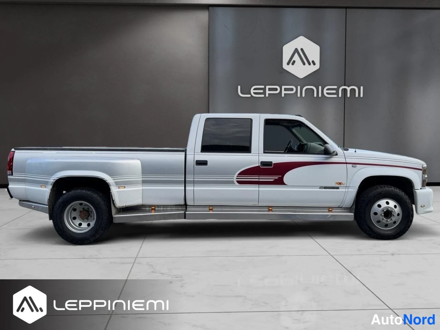 Sivulta: Chevrolet-pickup sivulta valokuvattuna; valkoinen koritoni varusteena viininpunainen koristemaalaus, neljä ovea ja kaksoistakapyörät.