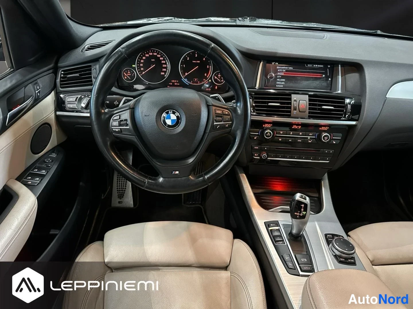 Muu: Ohjaamon näkymä tuulilasista:BMW-ohjauspyörä, instrumentit, keskikonsolin vaihtaja ja infonäyttö, beiges istuimet.