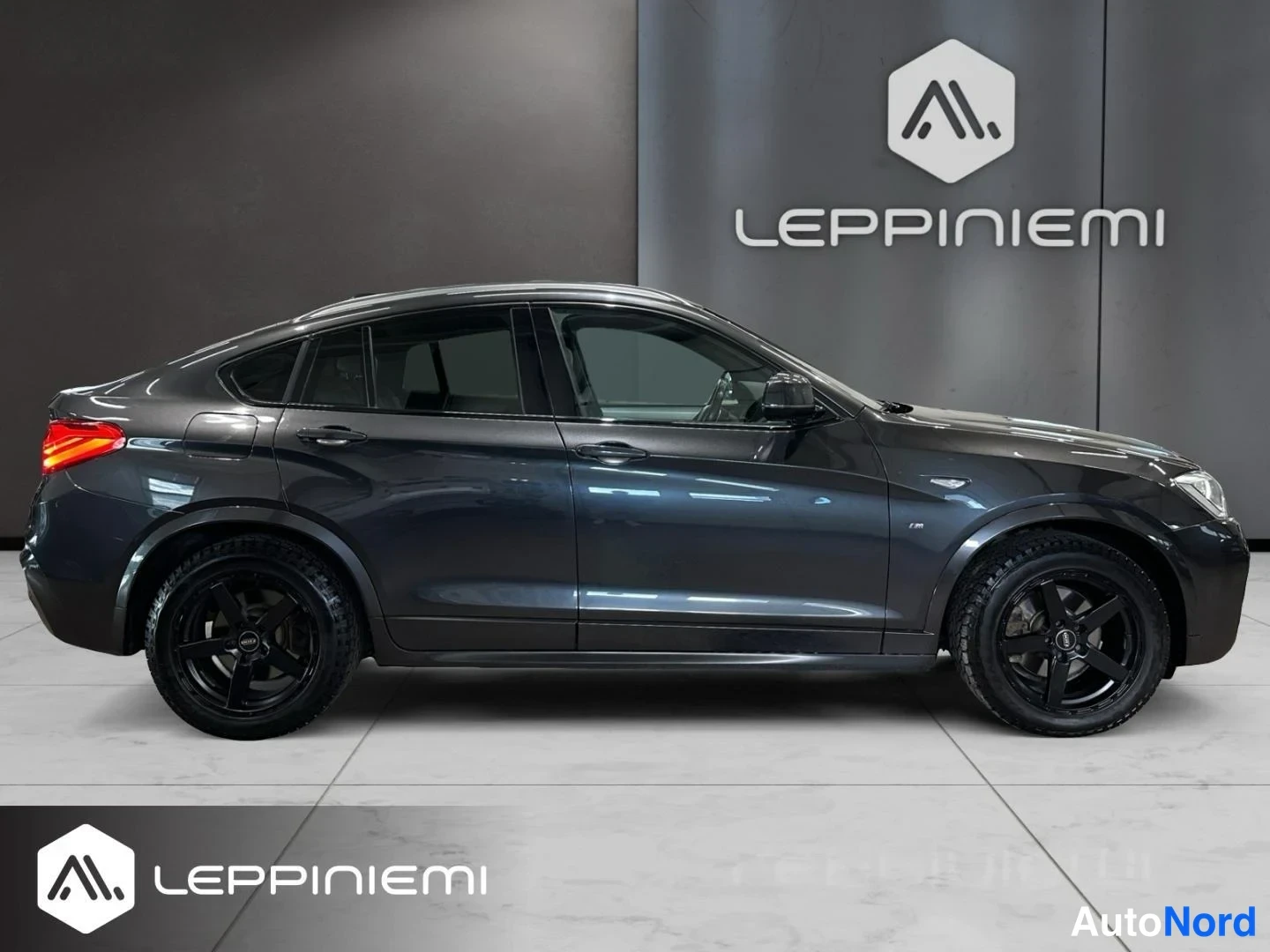 Sivulta: BMW X4:n sivunäkymä oikealta puolelta sisätiloissa; tummanharmaa koripinta, mustat kevytmetallivanteet, takavalot ja kattokaiteet näkyvät.