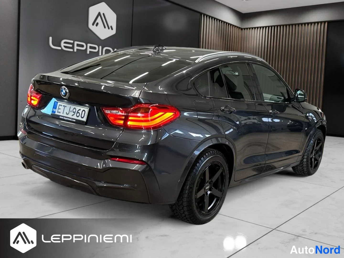 Takaviisto: Auton takakolmasosanäkymä: tummanharmaa BMW-urheilumaasturi, rekisteritunnus, mustat kevytmetallivanteet ja katkaisimet paloivat.