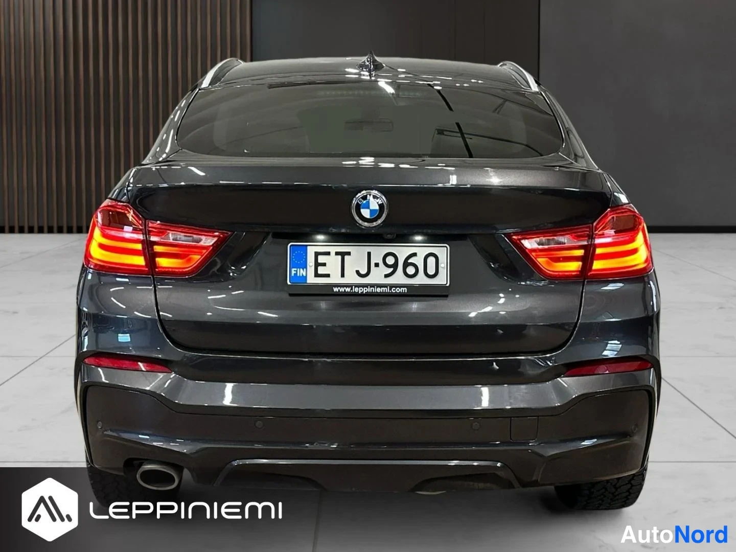 Takaa: Auton suora takanäkymä: tummanharmaa BMW, rekisteritunnus, kattospoileri ja tummat puskurit.