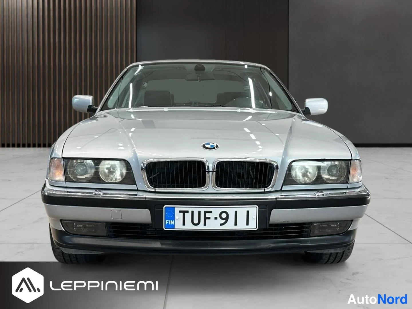 Edestä: Suora etunäkymä hopeanvärinen BMW 7 -sarjan sedan, kuvattu sisätiloissa, rekisteritunnus.