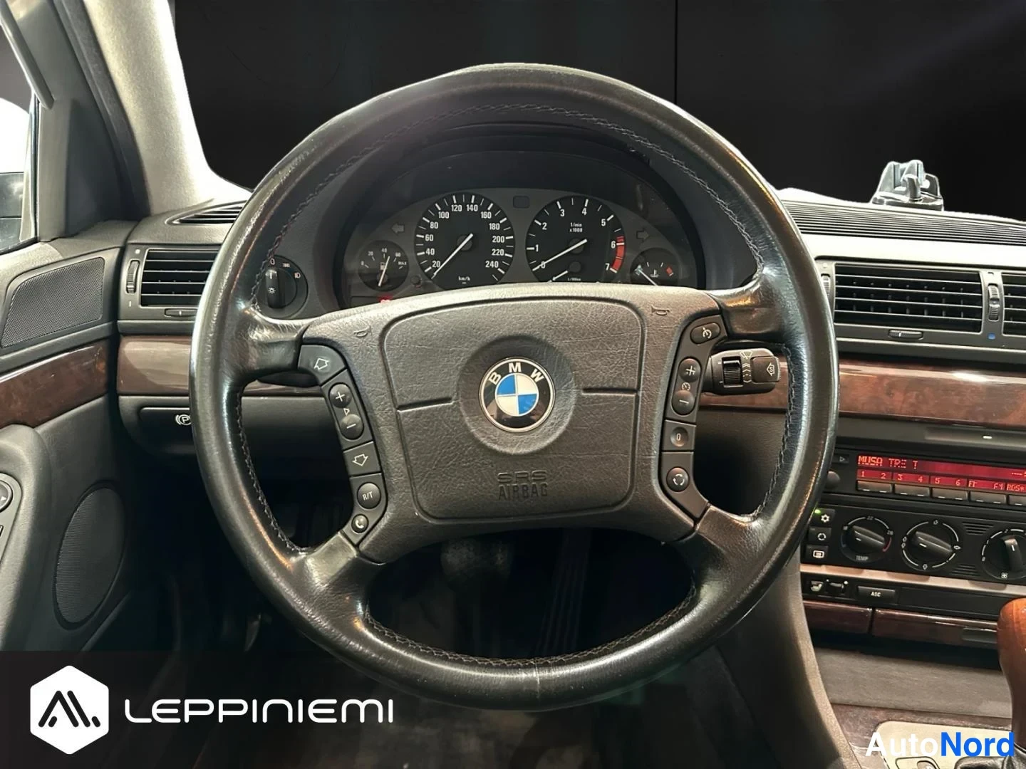 Muu: Ohjauspyörän lähikuva: BMW-merkki keskellä, SRS AIRBAG-teksti, monitoiminapit molemmin puolin ja mittaristo taustalla (100–240 km/h).