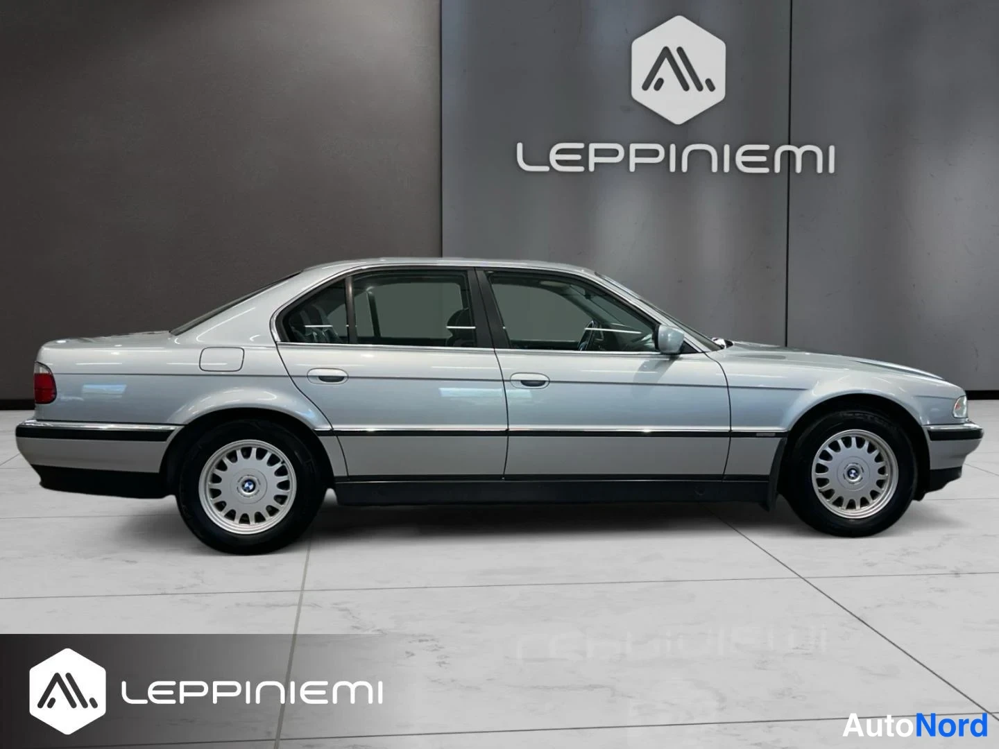 Sivulta: Kylkinäkymä hopeanvärinen BMW 7 -sarjan sedan, neliovinen, autonmyyntitilassa kuvattuna.