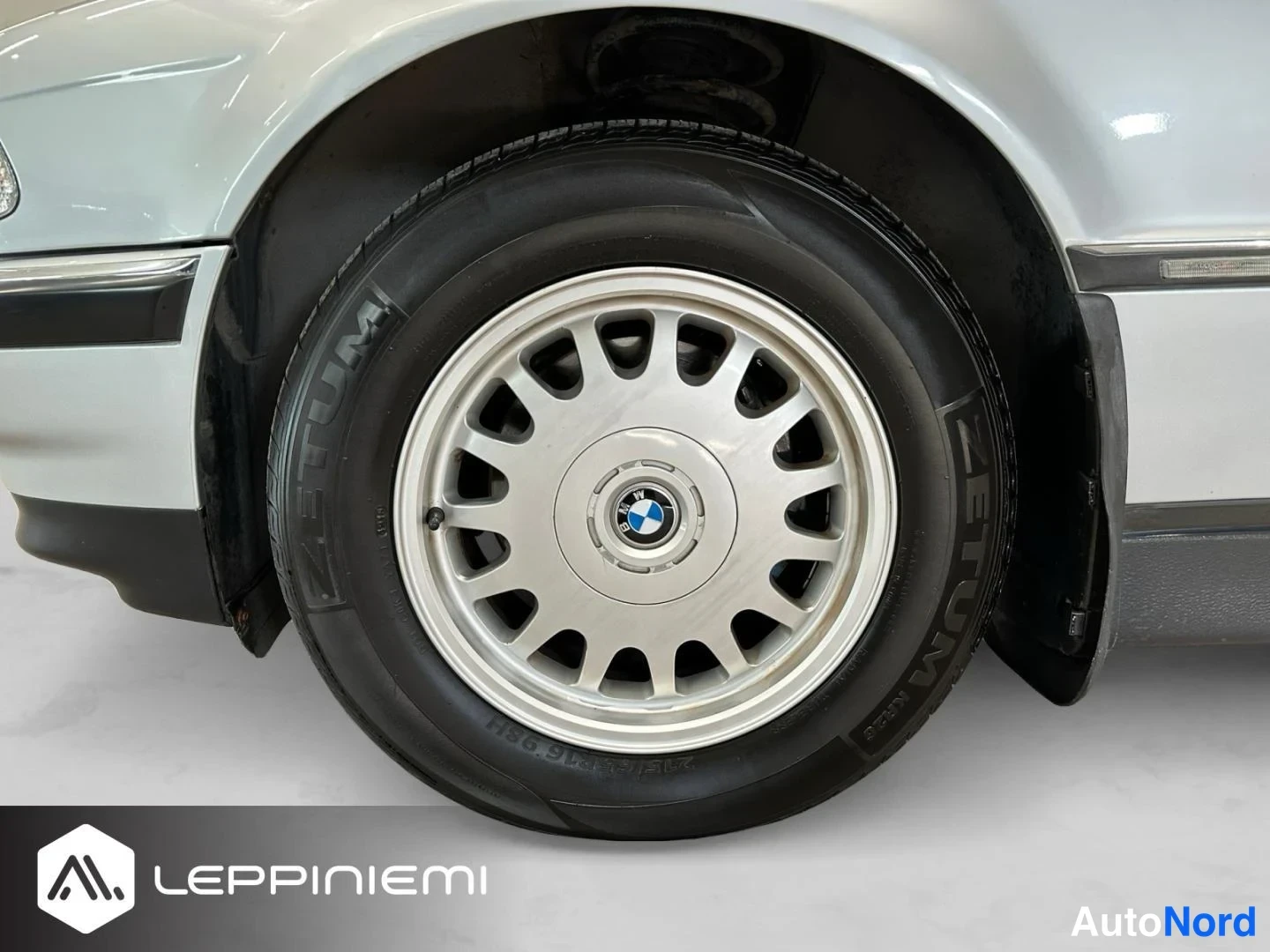 Sivulta: Sivukuva auton etupyörästä lähikuvana: hopeinen vanteen keskellä BMW-merkki, musta Zetum-rengas ja vaaleaa koria.