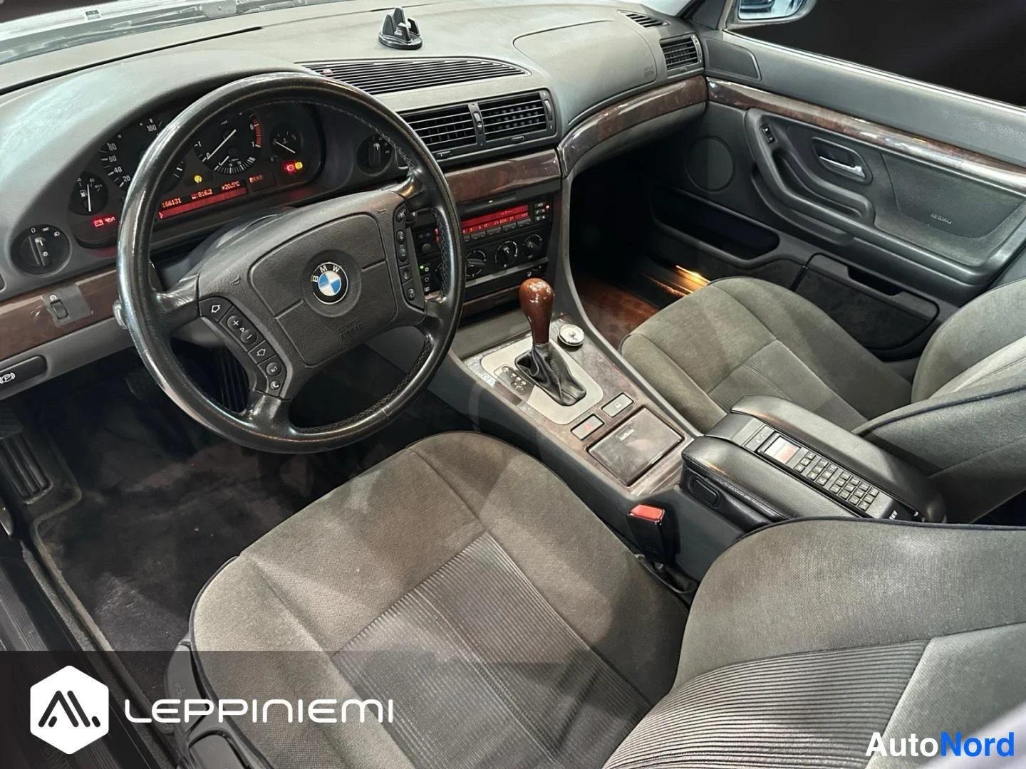 Muu: Sisätila kuljettajan puolelta: BMW:n ohjauspyörä ja kojelaudan mittarit, tumma kangasverhoilu, puukoristeet, automaattivaihteen valitsin ja kesäkäytävän säilyty