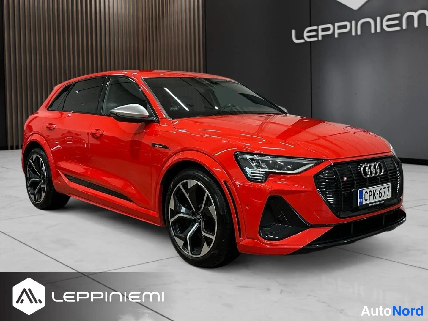 Etuviisto, nokka oikealle: Audi e-tron -maasturin punaisen korin etukolmannellinen kuva vasemmalta, musta etusäleikkö ja -rekisterikilpi näkyvät.