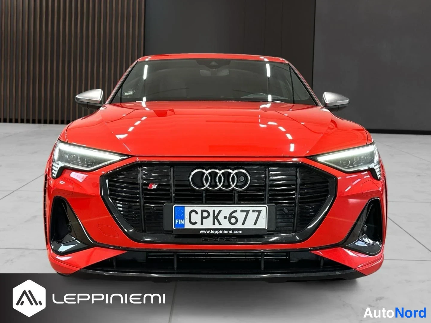 Edestä: Punaisen Audi e-tronin suora etunäkymä, musta säleikkö, Audi-merkki ja -rekisterikilpi.