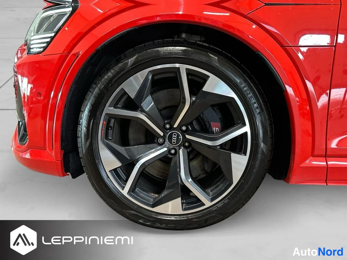 Edestä: Punaisen Audi e-tronin etupyörän lähikuva; tumma kolmiagenttinen tai kaksiosainen kevytmetallivanne, Pirelli-rengas ja punainen jarrusatu näkyvät.