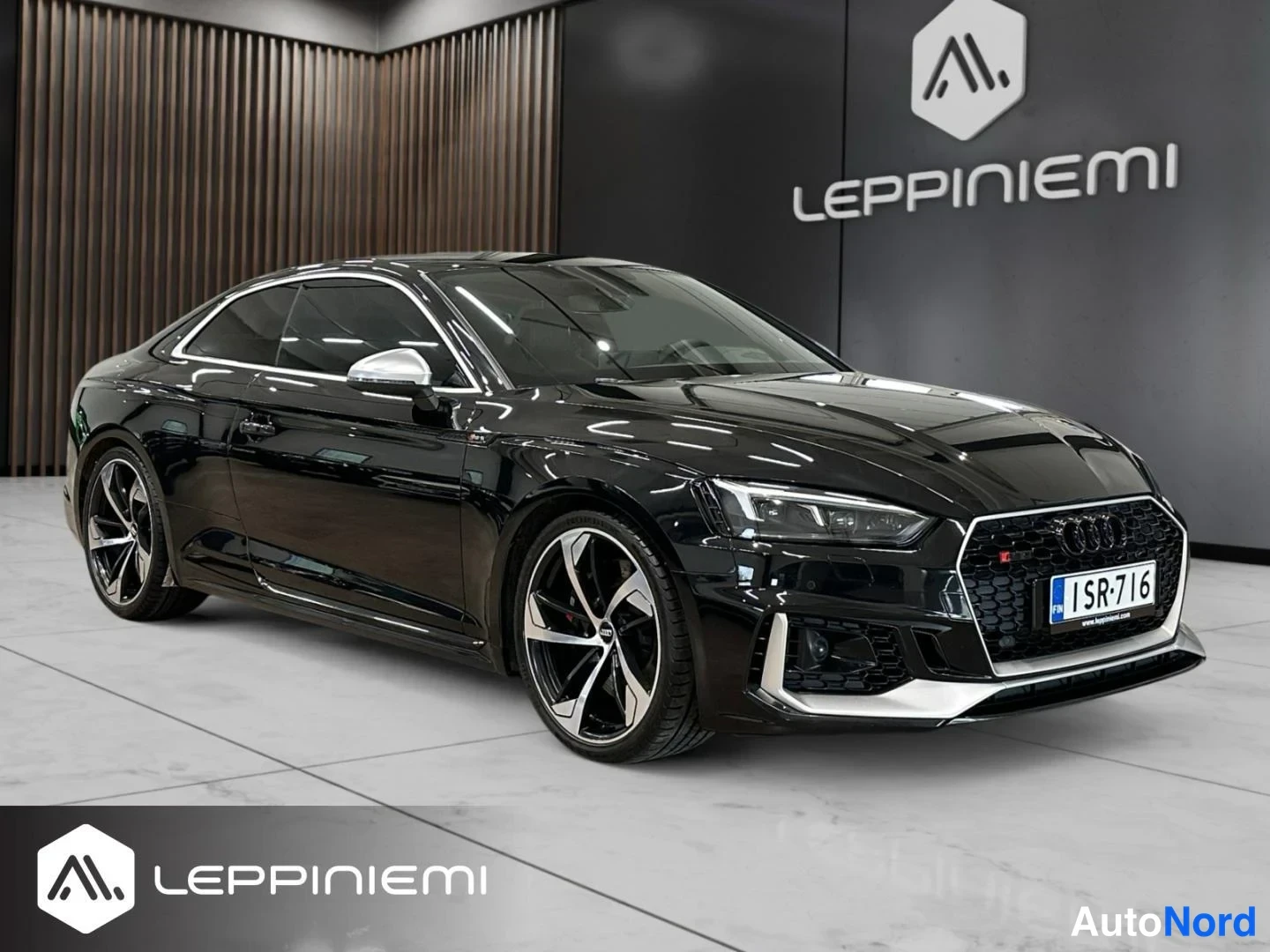Etuviisto, nokka oikealle: Mustan Audi RS5 Coupé -auton etukulma ilmastointikaapissa, etusuoja ja rekisterikilpi näkyvissä.