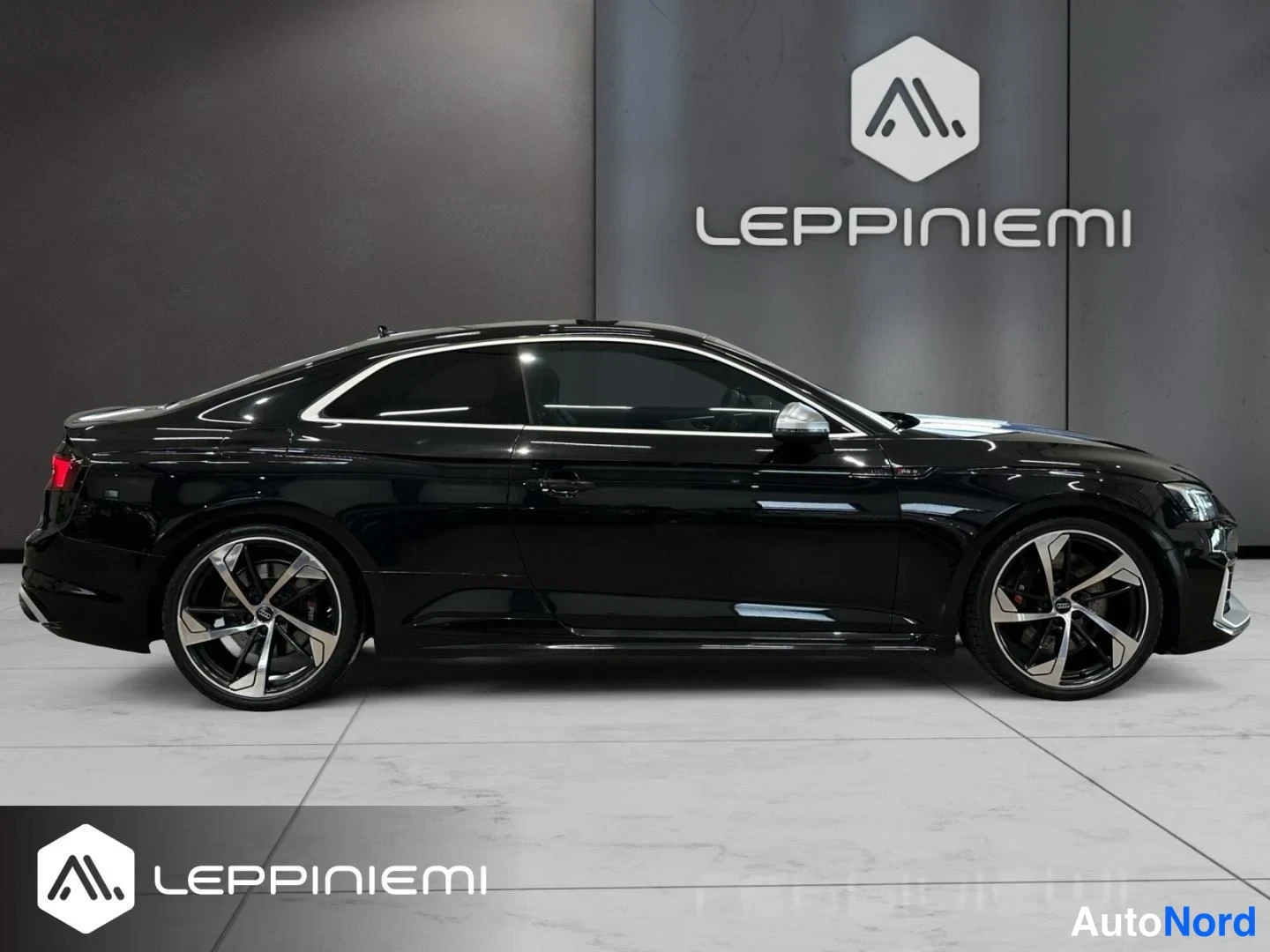 Etuviisto, nokka oikealle: Mustan coupé-auton sivuprofiili showroomissa, keula lievästi oikealle kääntyneenä, suuret kevytmetallivanteet.