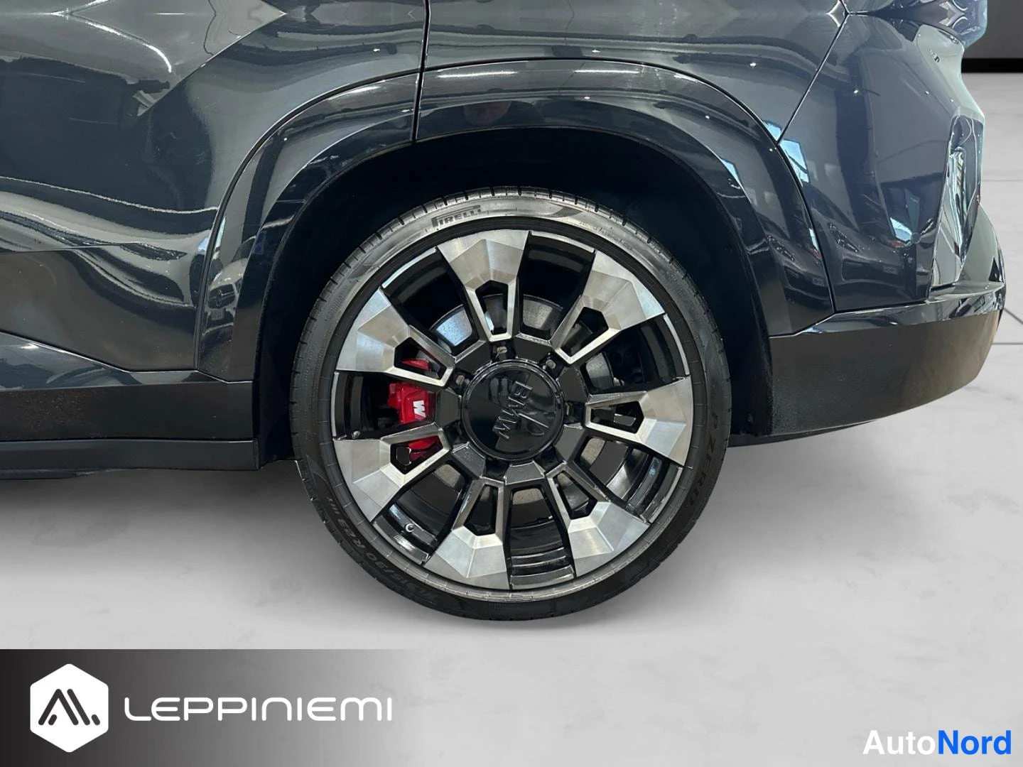 Sivulta: Sivukulmakuva mustan auton takapyörästä: tumma metallivanne, punainen jarrusatula ja Pirelli-rengas.