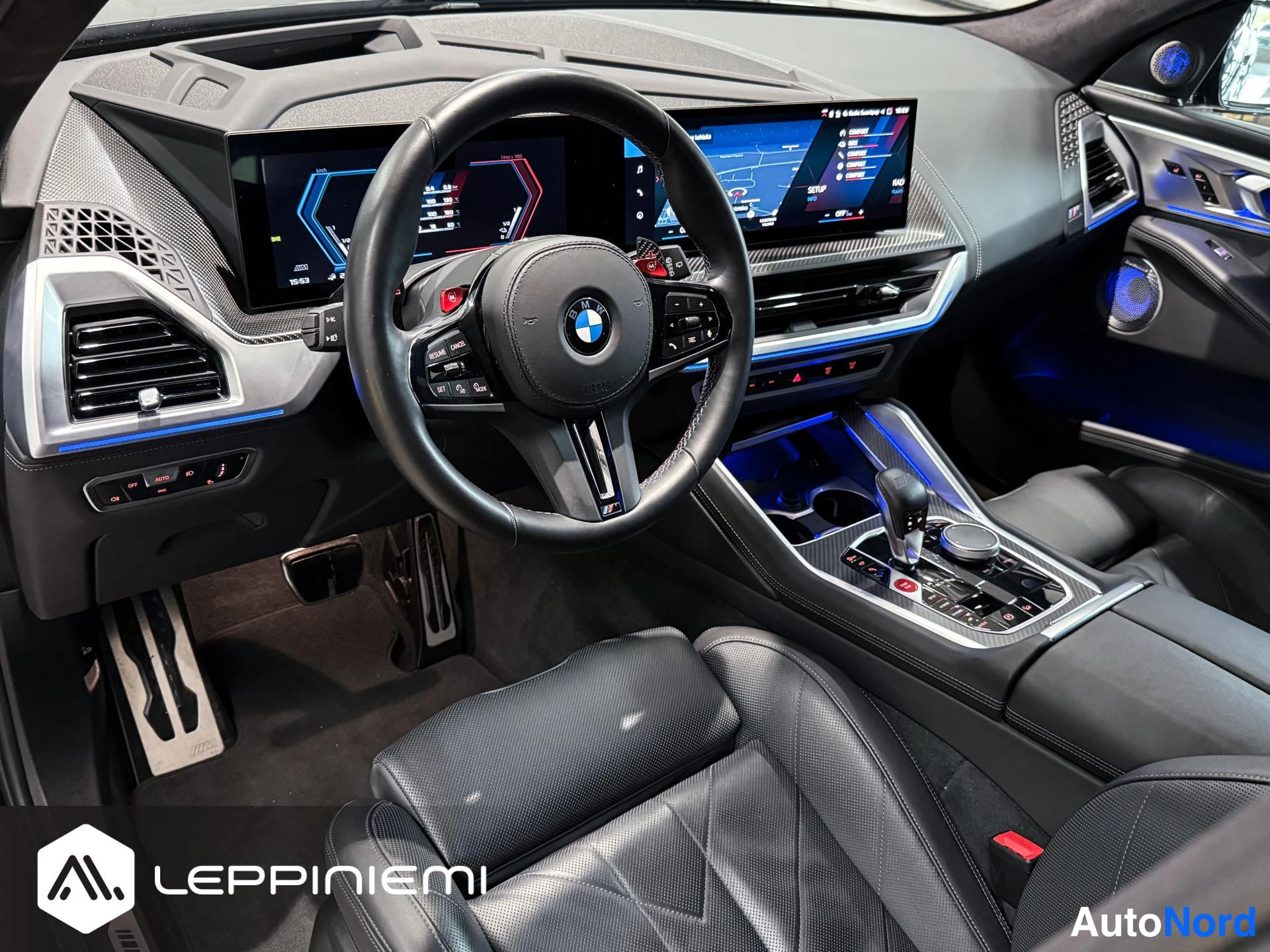 Muu: Kojelaudan etunäkymä: BMW-M-ohjauspyörä, kaksi erillistä näyttöä, hiilikuitukoristeet ja sininen sisävalaistus.