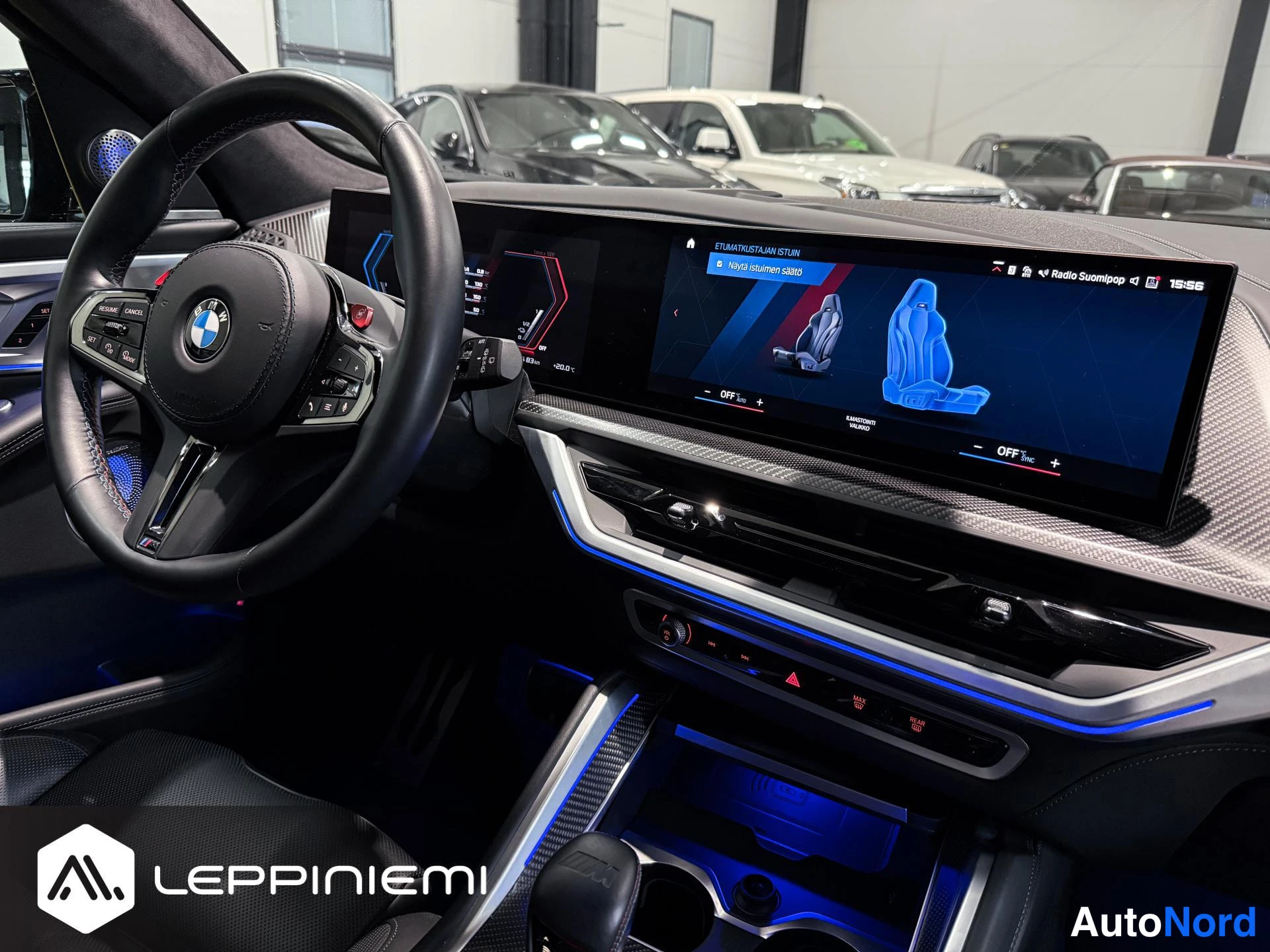 Yksityiskohta: Ohjaamo kuljettajan puolelta: BMW-ohjauspyörä, pitkä kosketusnäyttö, jossa suomalainen käyttöliittymä, ja sininen ympäristövalaistus.