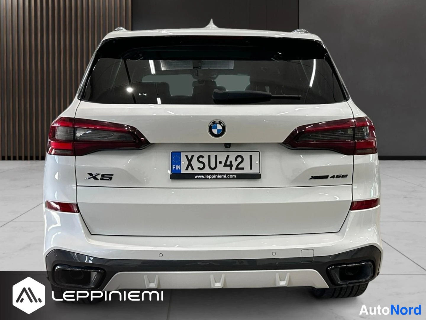 Takaa: Valkoisen BMW X5:n takaosa suoraan takaa, rekisteritunnus (FIN), X5- ja 45e-merkit, tumma diffuusori ja kattotelineet.