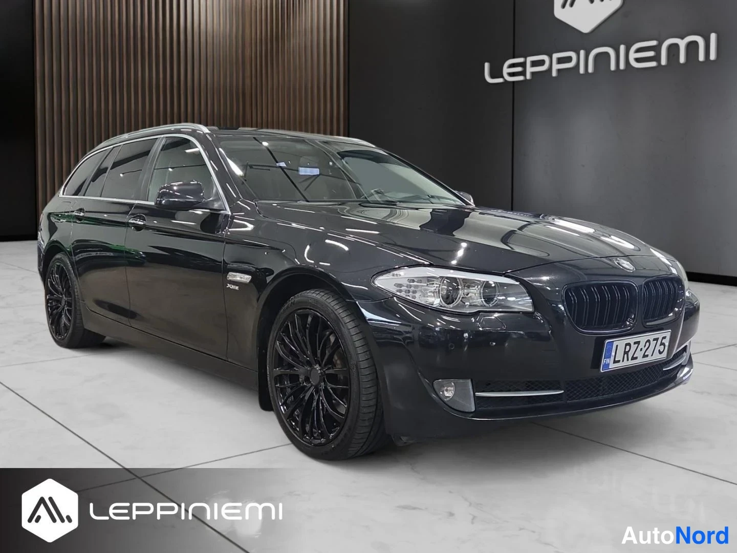 Etuviisto, nokka oikealle: Mustan BMW 5 -farmarin etukulman sisätiloissa; rekisteritunnus ja mustat vanteet.