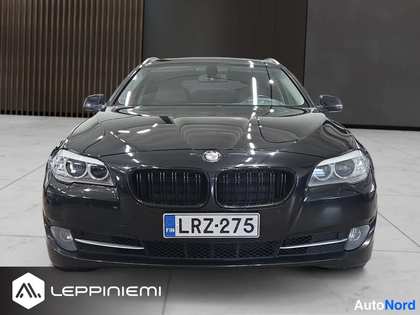 Edestä: Mustan BMW:n etunäkymä sisätiloissa; rekisteritunnus.