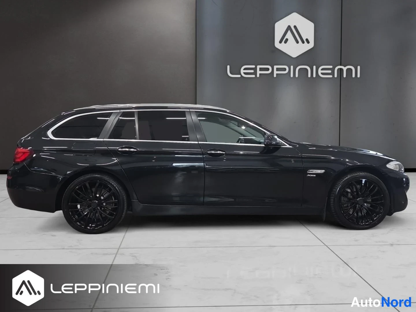 Sivulta: BMW 530 Touring -farmariauto sivusta, musta kori ja mustat kevytmetallivanteet kuvattuna sisätiloissa.