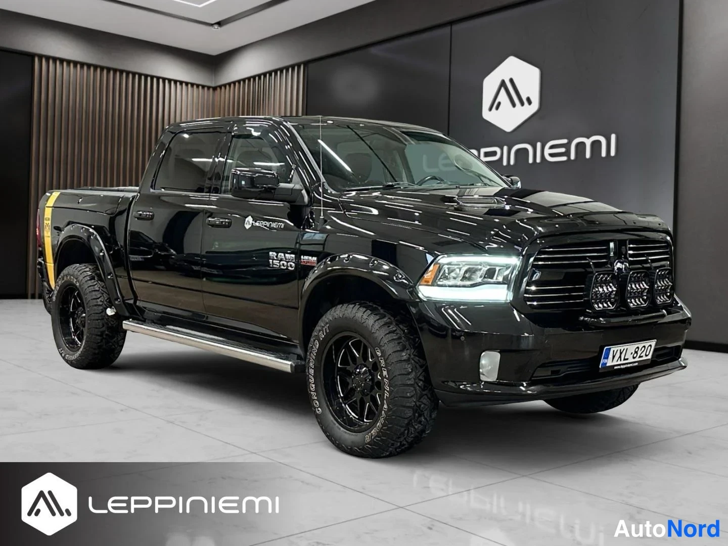 Etuviisto, nokka oikealle: Musta nelioveto Ram 1500 -lainen lava-auto etukulmasta oikealta, lisävaloja puskurissa.