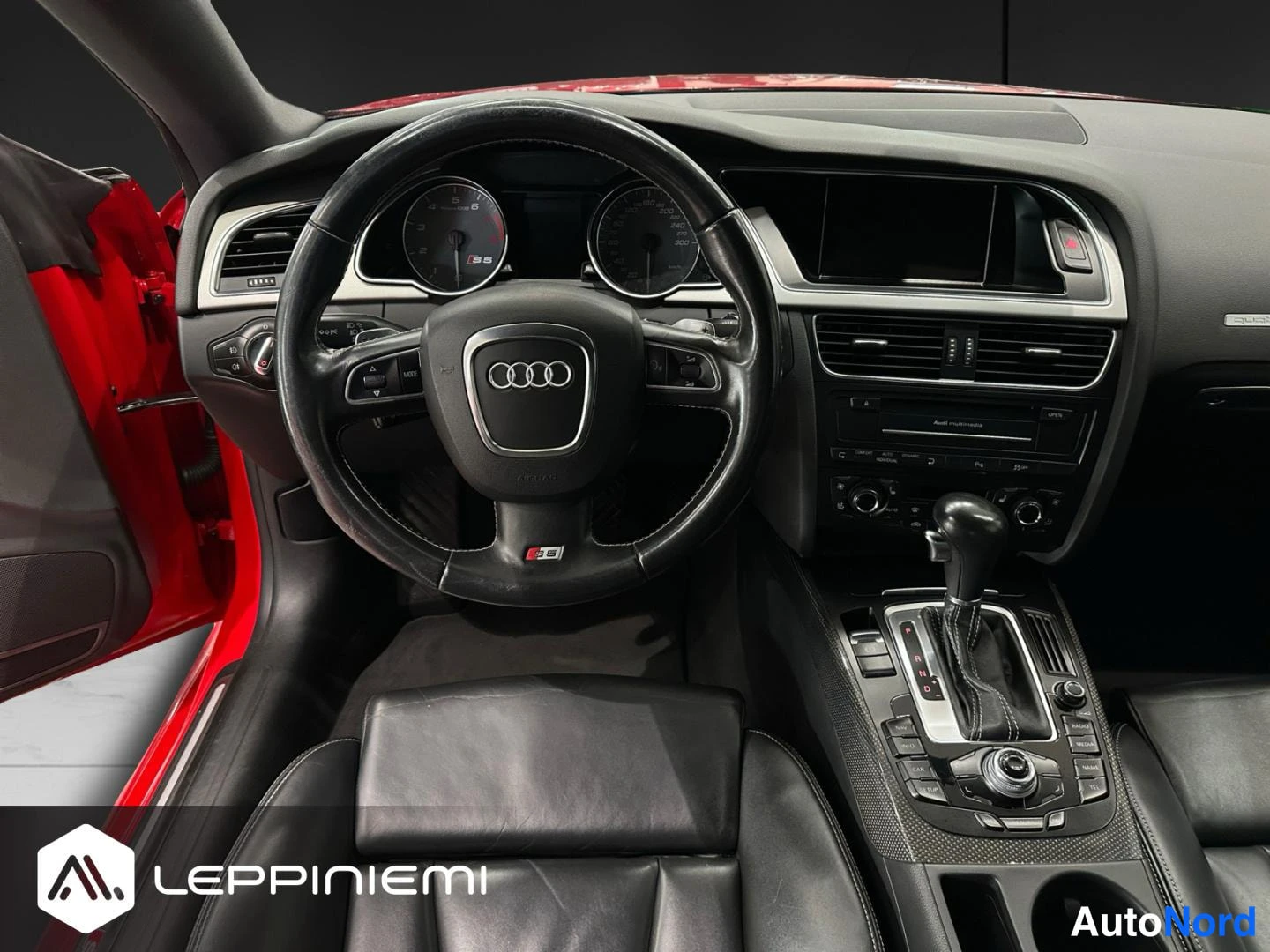 Muu: Ohjaamo suoraan edestä: Audi-ohjauspyörä S5-merkillä, mittaristo ja automaattivaihteen vaihtaja