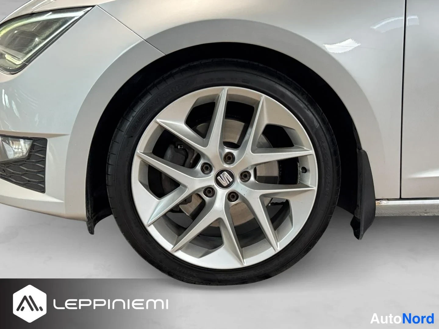 Etuviisto, nokka vasemmalle: Lähikuva Seatin hopeanharmaan auton etupyörästä; kevytmetallivanne ja Seat-merkki napassa.
