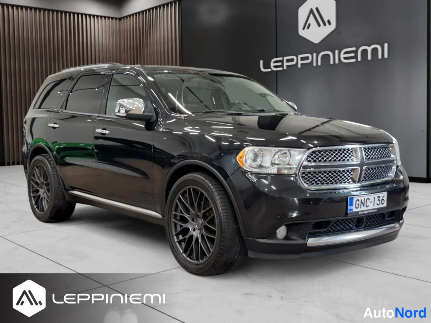Etuviisto, nokka oikealle: Musta Dodge Durango -maast-auto kolmannelta etukulmalta sisätiloissa, korostunut etusäleikkö ja mustat kevytmetallivanteet.