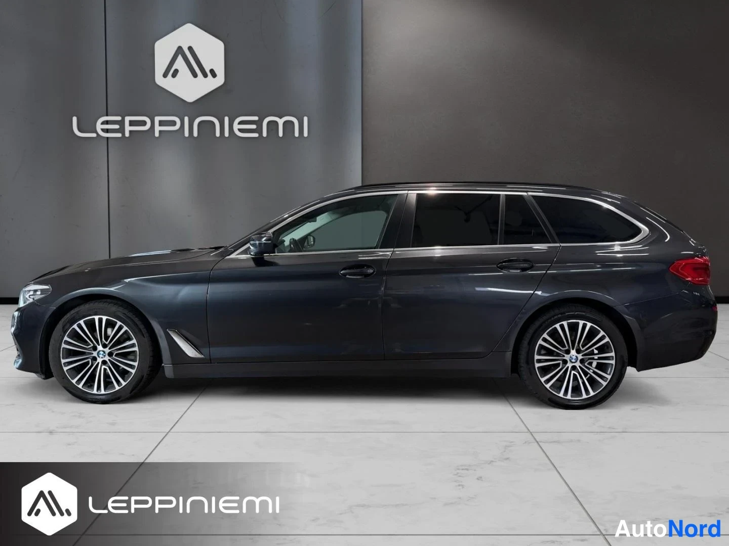 Takaviisto: BMW 520 Touring -farmarin takaosan ja sivun profiilinäkymä, tummanharmaa kori ja takavalot osittain näkyvillä.