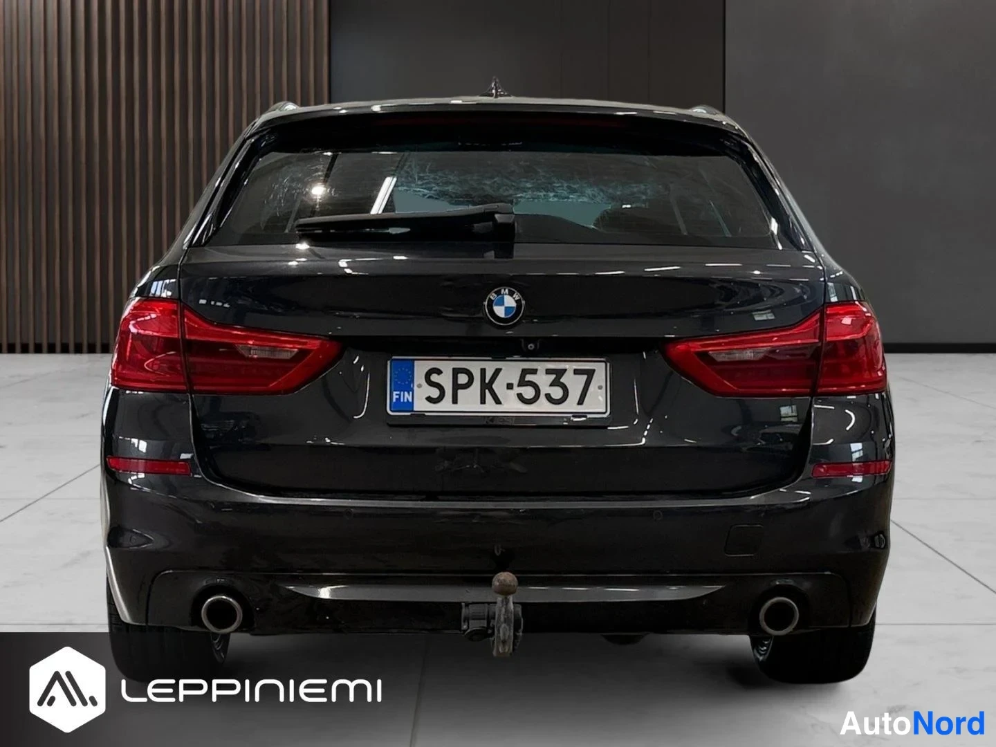 Takaa: BMW 5-sarjan farmari suoraan takaa; rekisterikilpi, punaiset takavalot, kaksi pakoputkea ja vetokoukun pallo näkyvät.
