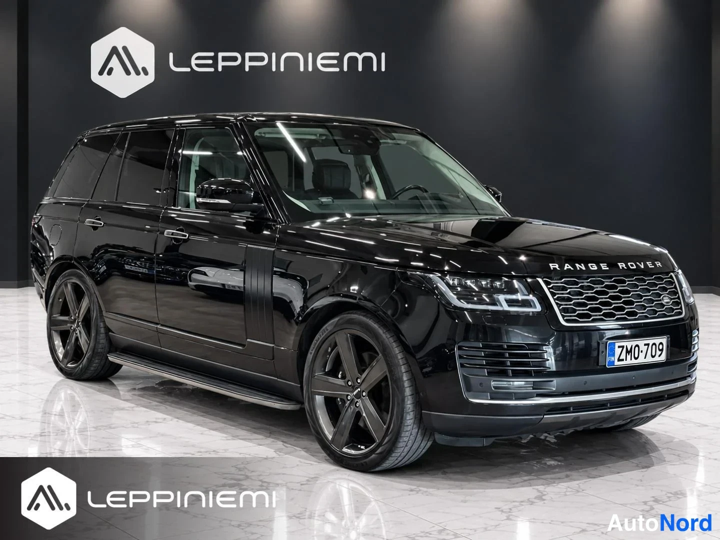 Etuviisto, nokka oikealle: Musta Range Rover -maastauto kolmasosan etunäkymässä nokka oikealla, rekisterikilpi ZM0-709, showroomissa.