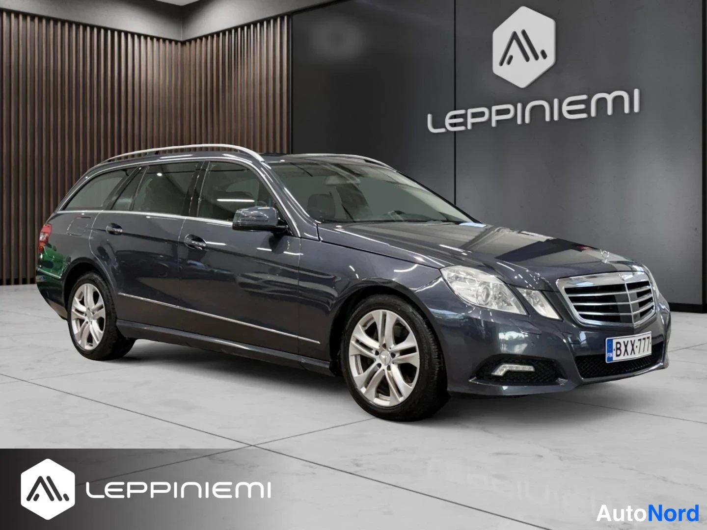 Etuviisto, nokka oikealle: Tummansininen Mercedes-Benz farmari etukulmasta, keulapuskuri ja rekisterikilpi BX-777 näkyvät.