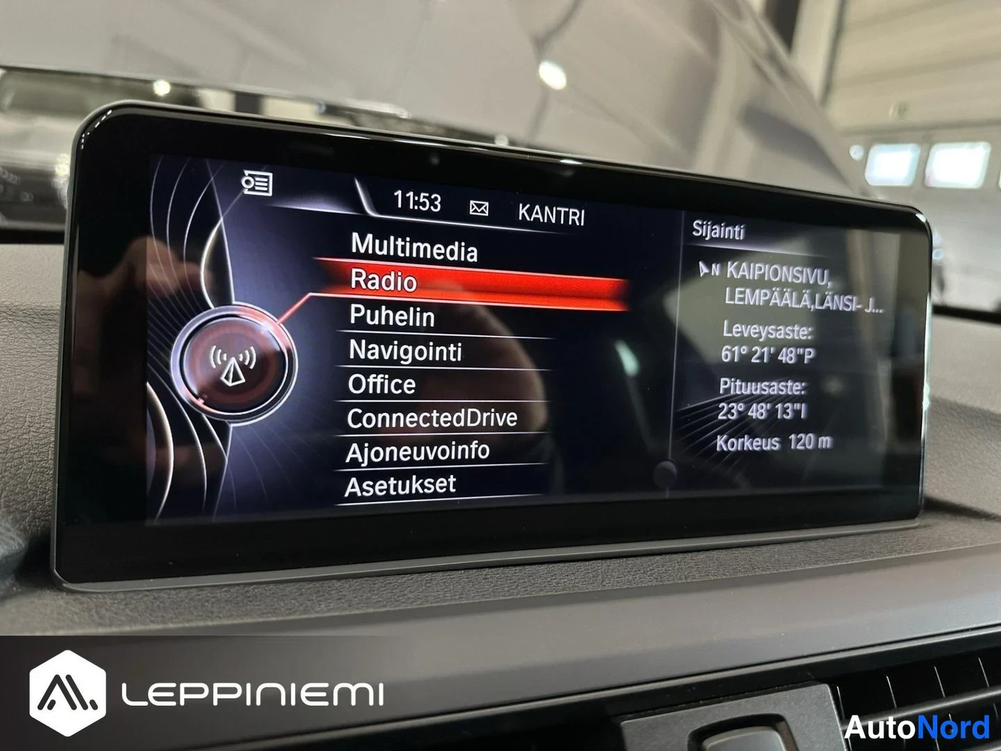 Muu: Auton infotainment-näytön kuva: valikko Radio valittuna, kohdat Multimedia, Puhelin, Navigointi, Office, ConnectedDrive, Ajoneuvoinfo ja Asetukset; oikealla sij