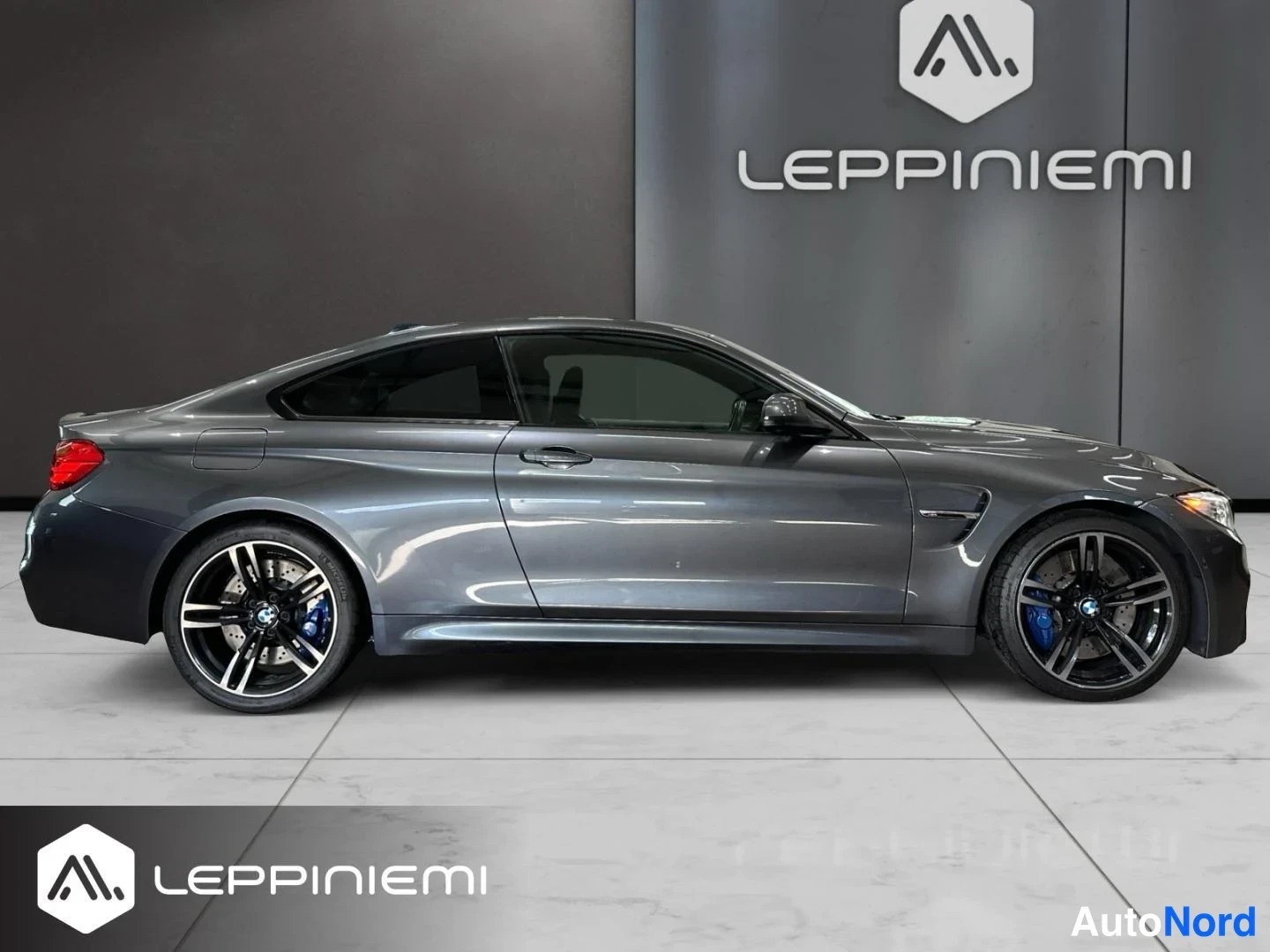 Sivulta: BMW M4 -kupé sivulta, tummanharmaa koripaneeleihin, mustat monipuoliset alumiinivanteet, siniset jarrusatulat näkyvät sekä etu- että takaosassa.