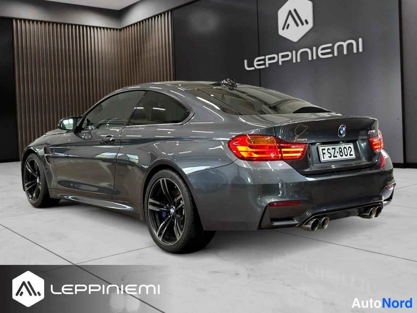 Takaviisto: Auton takakolmannellinen näkymä sisätiloissa: tummanharmaa BMW-coupé, rekisteritunnus, neljä pakoputkea ja mustat kevytmetallivanteet.