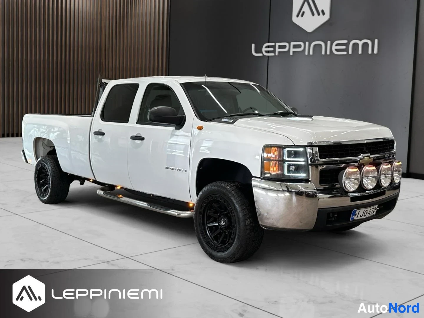 Etuviisto, nokka oikealle: Valkoinen Chevrolet Silverado 3500 HD -nakkuauto neljäovinen etukulmasta oikealta, kromiset lisävalot ja mustat kevytmetallivanteet.