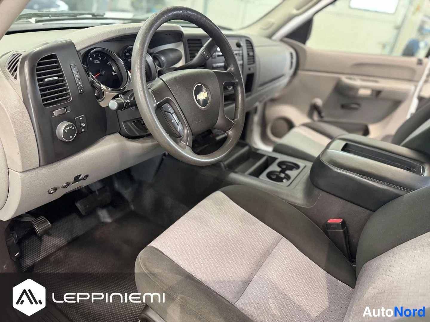 Muu: Ohjaamo sivusuunnassa: ohjauspyörä Chevrolet-tunnuksella, kojelauta, istuimet ja keskikonsolin kuppiastiat.