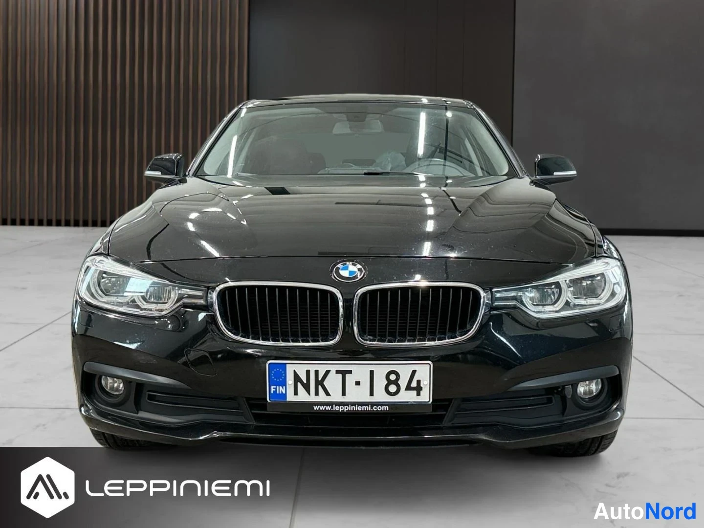 Edestä: Mustan BMW-sedanin suora etunäkymä; näkyvät etumousto, ajovalot ja rekisterikilpi.