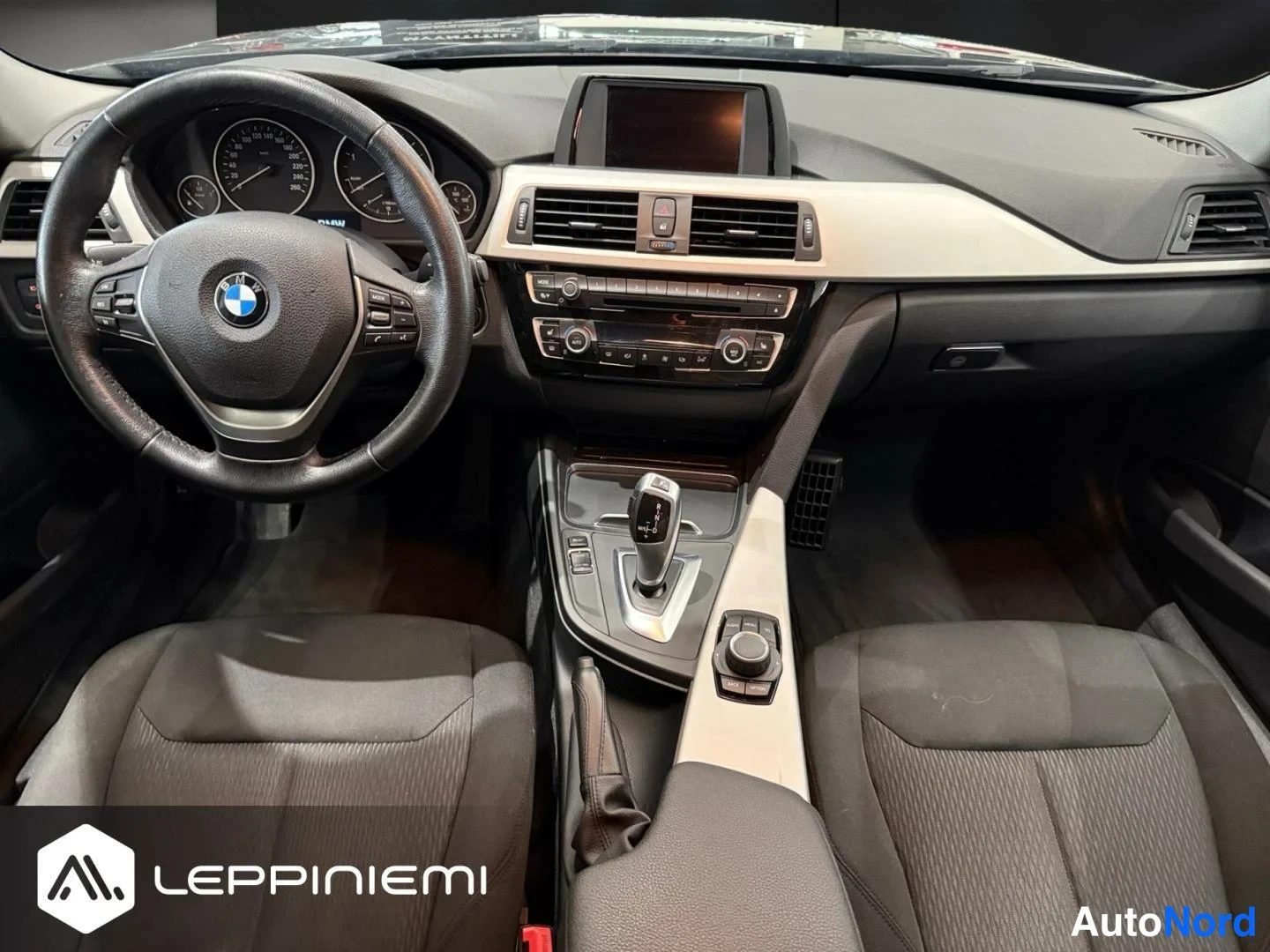 Edestä: Kojelauta suoraan edestä: BMW-ohjauspyörä, mittarit, keskinäyttö ja automaattivaihteisto.