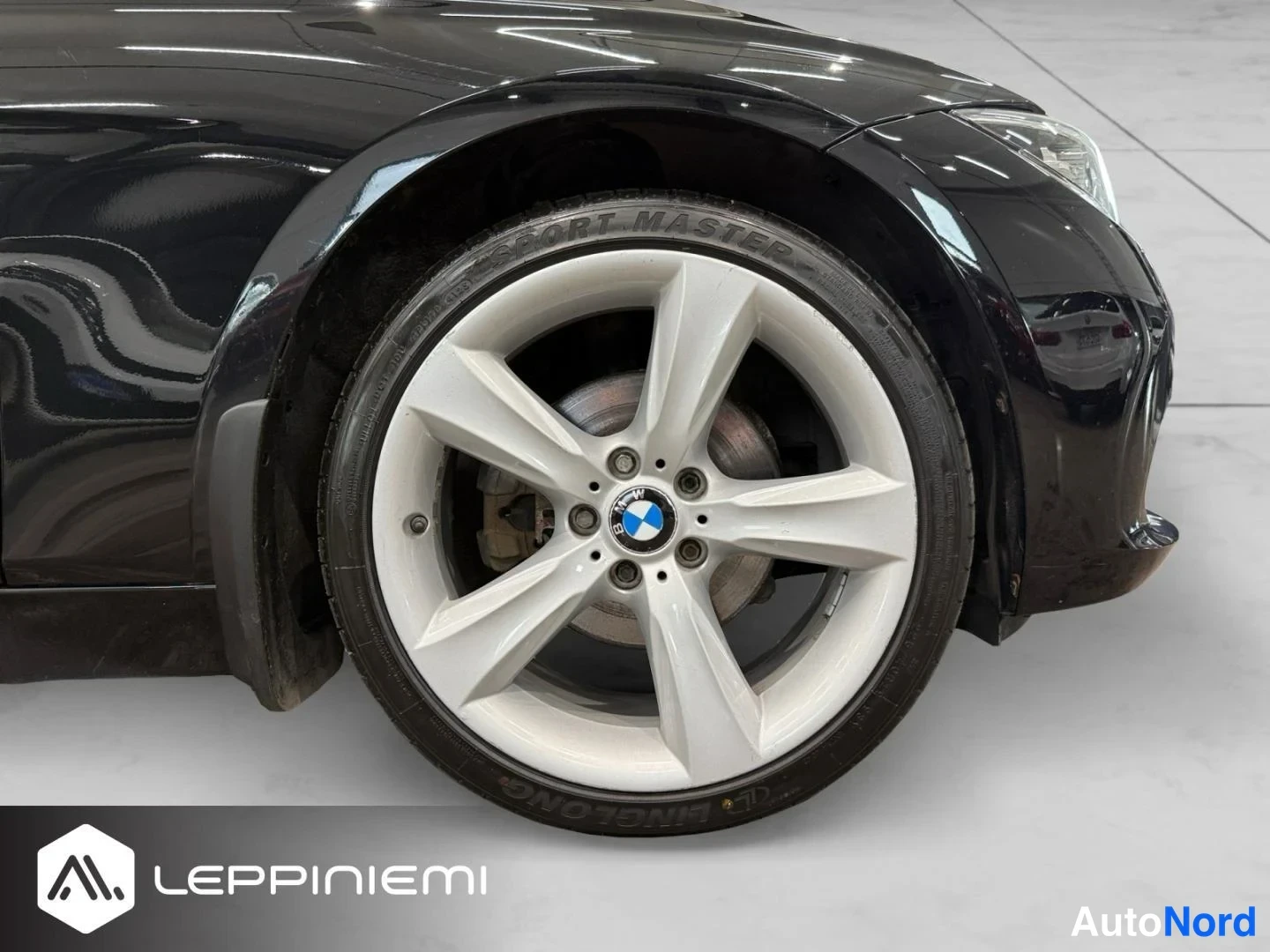 Edestä: Etupyörän lähikuva: hopea viisipuolinen BMW-kehävanteen ja musta lumipatsas, etusuoja näkyvissä.