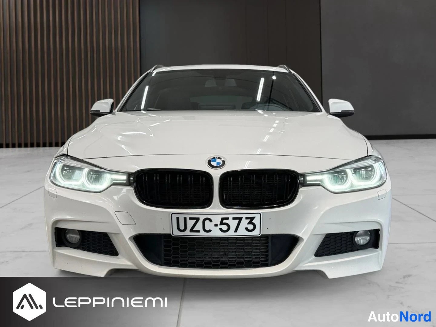 Edestä: Valkoisen auton etunäkymä suoraan edestä; musta etusäleikkö ja BMW-merkki, rekisteri.