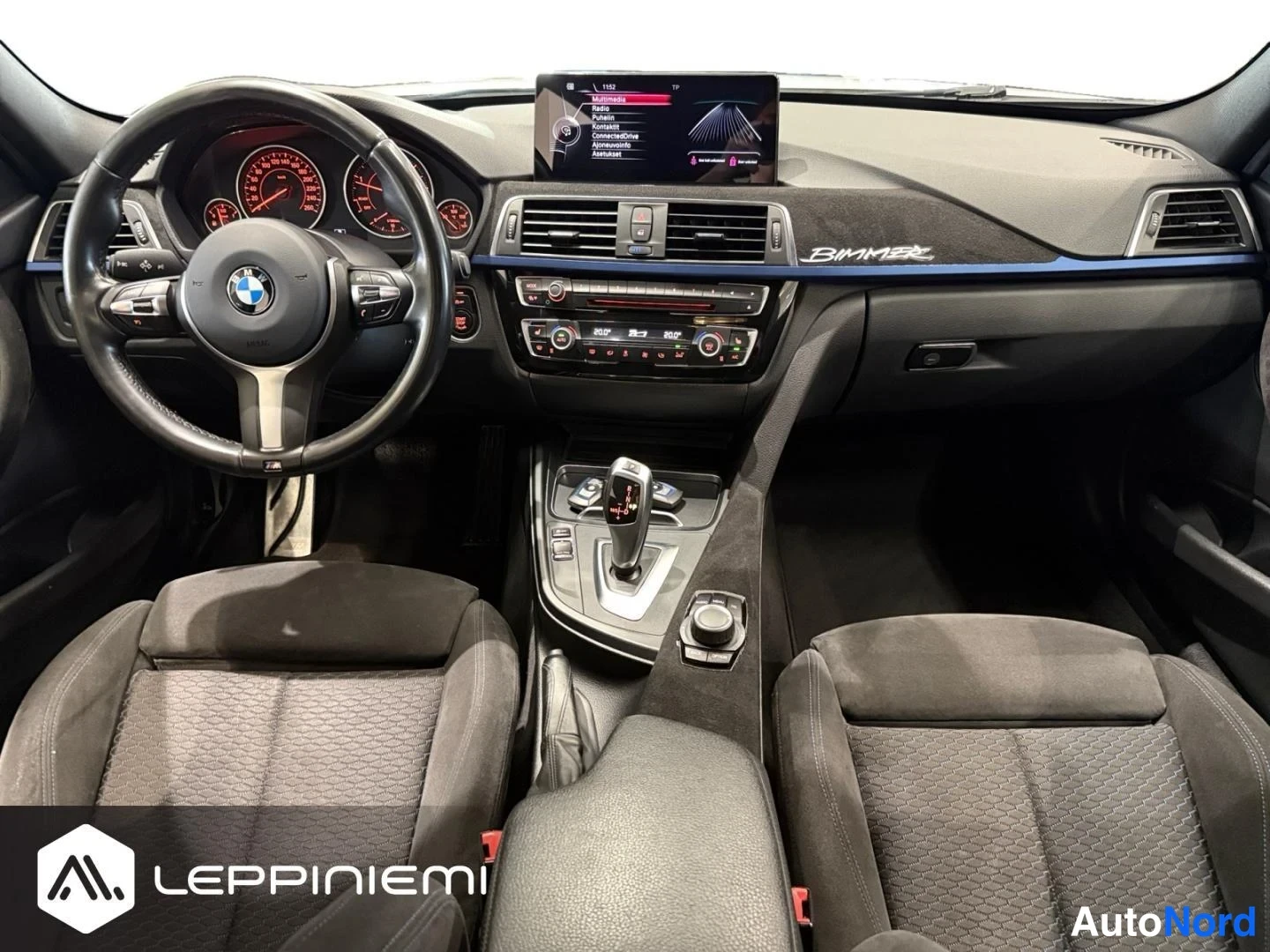Yksityiskohta: Auton sisätilat: BMW-ohjauspyörä, automaattivaihteen valitsin, näyttö kojelaudassa ja tummat urheiluistuimet.