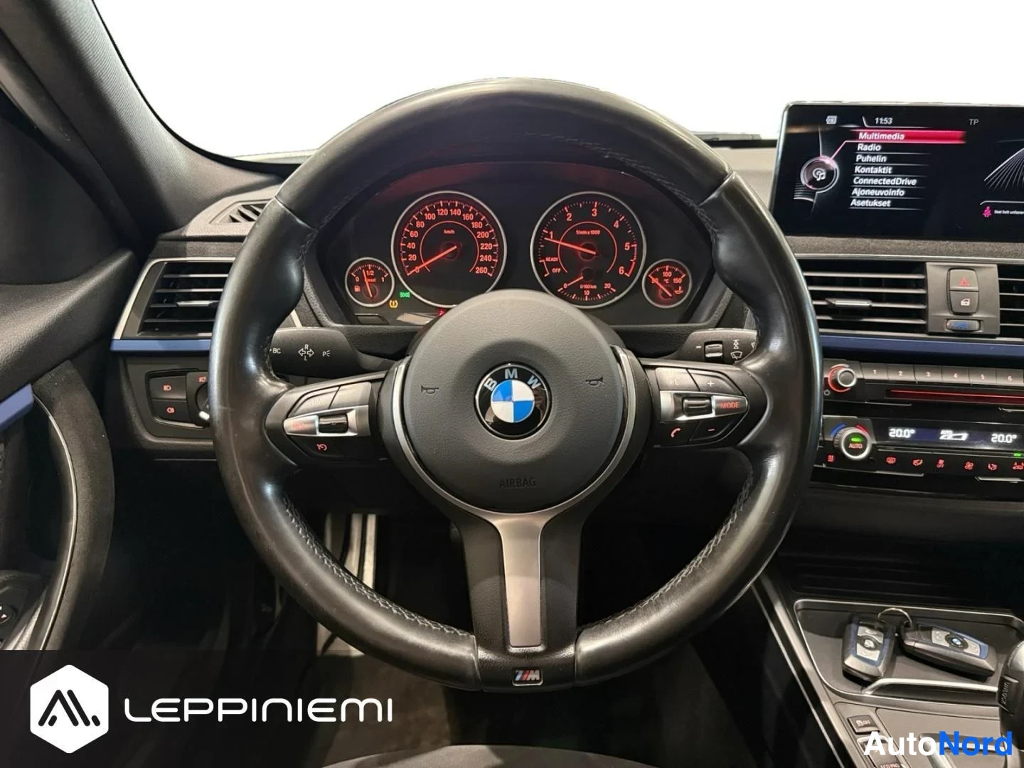 Yksityiskohta: BMW-ohjauspyörä, analogiset mittarit, keskikäyttöpaneeli ja infotainment-näyttö valikoilla Multimedia, Radio, Puhalin.